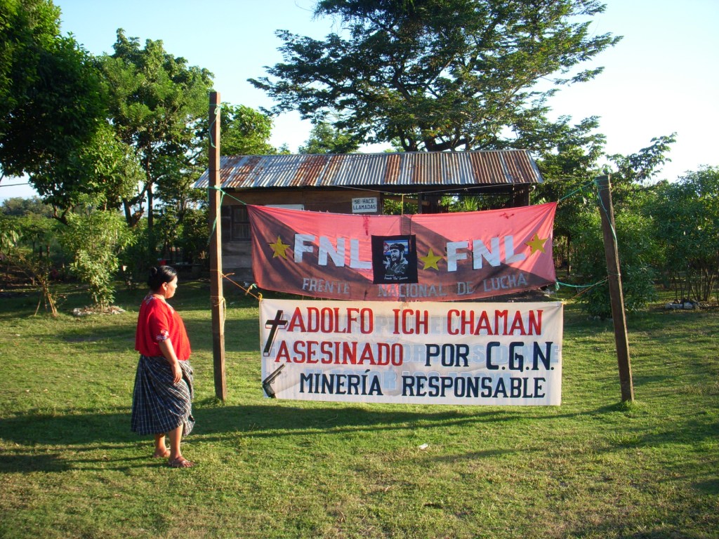 Angelica Choc stands next to a sign that says “Adolfo Ich murdered by CGN. Mining is responsible.”  Photograph by Daniel Sosa
